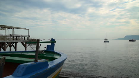Slow-pullback-beside-colorful-wooden-fishing-boat-on-shore-of-calm-bay