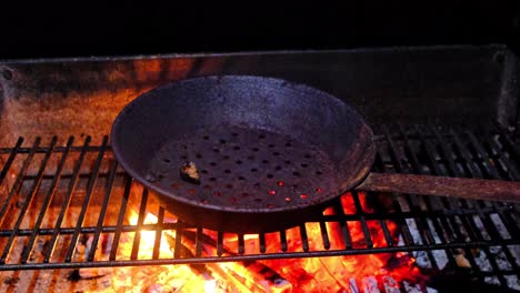 Rusty-perforated-chestnut-cooking,-roasting-pan-on-opem-fire,-close-up,-dark-barckground