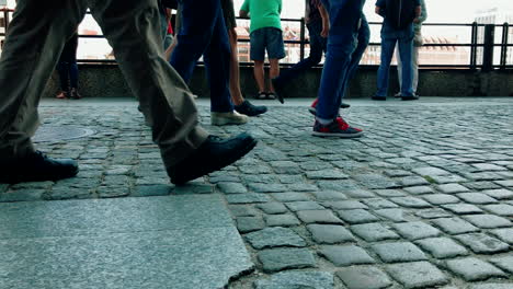 People-walk-on-a-crowded-sidewalk,-close-up-view-of-the-sidewalk-and-legs-to-knee-height,-slow-motion-on-shoes-and-footsteps