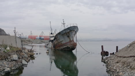 Rusty-grey-half-submerged-shipwreck-anchored-near-the-shore-on-a-cloudy-overcast-day