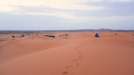Hombre-Berebere-En-El-Horizonte-Con-Manada-De-Camellos-Caminando-En-El-Desierto-Del-Sahara,-Marruecos