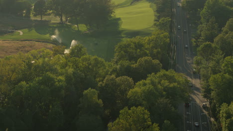 Überfliegen-Sie-Einen-Golfplatz-Und-Eine-Nahe-Gelegene-Straße-Bei-Sonnenuntergang-Mit-Laufenden-Sprinkleranlagen