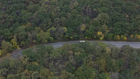 Follow-up-shot-of-a-bus-passing-on-a-two-lanes-asphalt-road-in-the-midst-of-an-autumn-forest