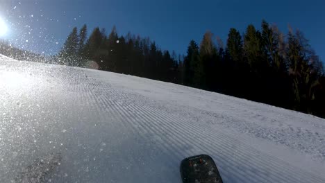 Ein-Skifahrer,-Der-Einen-Steilen-Hang-Hinunterfährt,-Im-Hintergrund-Ein-Blauer-Himmel-Mit-Strahlender-Sonne-Und-Schnee,-Der-Von-Den-Skiern-Aufsteigt-Blick-Vom-Rücken-Des-Skifahrers