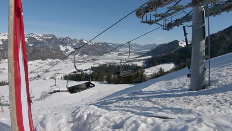 Panoramic-shot-of-a-ski-lift-moving-uphill-with-skiers,-in-the-background-a-panorama-of-a-snowy-valley-and-mountain-peaks