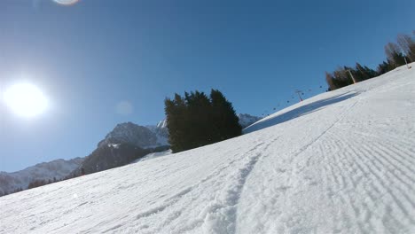 Un-Esquiador-Bajando-Una-Pendiente,-En-El-Fondo-Un-Cielo-Azul-Con-Sol-Brillante-Y-Vista-Del-Telesilla-Desde-La-Espalda-Del-Esquiador