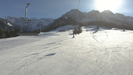 Hyperlapse-Von-Einem-Skilift,-Der-Mit-Skifahrern-Im-Hintergrund-Schneebedeckter-Berggipfel-Und-Strahlender-Sonne-Bergauf-Geht