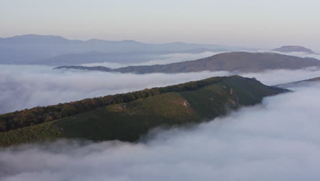 Cresta-De-La-Montaña-Con-árboles-A-Los-Lados-Rodeados-De-Densas-Nubes-De-Niebla-Al-Atardecer