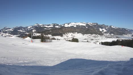Zeitraffer-Eines-Skilifts,-Der-Bergauf-Fährt,-Mit-Skifahrern-Und-Skifahrern,-Die-An-Einem-Sonnigen-Tag-Im-Hintergrund-Schneebedeckte-Berggipfel-Den-Hang-Hinunterfahren