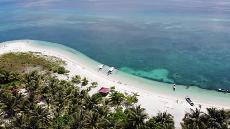 4K-aerial-rising-shot-of-secluded-beach-and-boats-looking-over-clear-blue-water-in-Balabac,-Palawan-Philippines