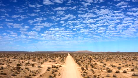 Flying-backward-over-desert-dirt-road-with-blue-sky-and-fluffy-clouds