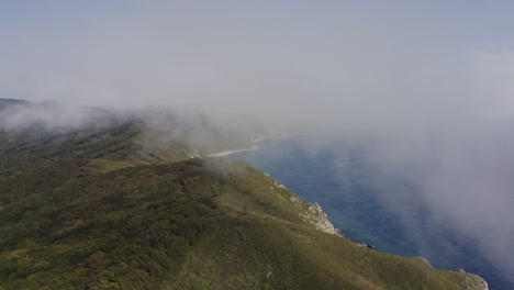 Bird's-eye-view-of-a-breathtaking-steep-rocky-coast-line-with-heavy-dense-fog-approaching-from-the-sea,-Far-east,-Russia,-Sea-of-Japan