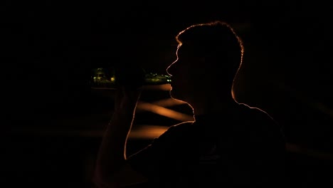 Mann-Trinkt-Nachts-Bier-Aus-Einer-Flasche-Unter-Einer-Straßenlaterne,-Die-Ihn-Als-Silhouette-Zeigt