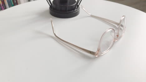 Moderne-Brillen-In-Heller-Farbe-Liegen-Auf-Einem-Weißen-Tisch,-Helles-Brillengestell,-Zeitlupenaufnahmen