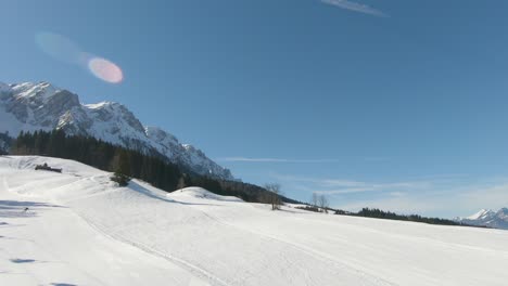 Panoramic-shot-taken-from-a-ski-lift-moving-uphill-with-skiers,-in-the-background-a-panorama-of-snowy-mountain-peaks