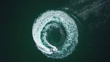 Aerial-bird-view-of-a-speedboat-riding-in-a-circle-and-making-beautiful-round-path-in-the-sea