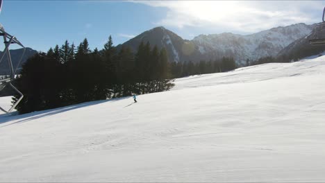 Schuss-Von-Einem-Skilift,-Der-Bergauf-Geht,-Mit-Skifahrern-Im-Hintergrund-Von-Schneebedeckten-Berggipfeln-Und-Skifahrern,-Die-Bergab-Gehen