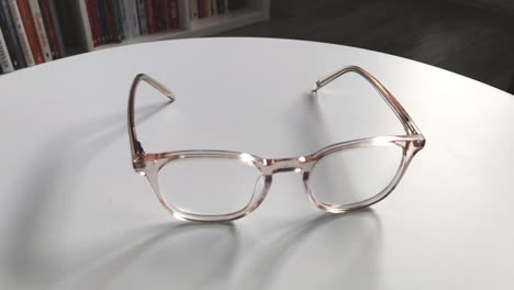 Modern-eyeglasses-in-light-colour-lie-on-a-white-table,-bright-glasses-frame,-slow-motion-footage