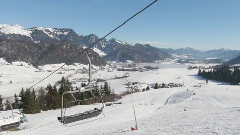 Panoramaaufnahme-Von-Einem-Skilift,-Der-Sich-Mit-Skifahrern-Bergauf-Bewegt,-Im-Hintergrund-Ein-Panorama-Auf-Ein-Verschneites-Tal-Und-Berggipfel