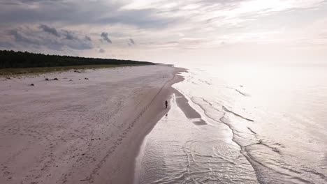 Aerial-Shot-of-Man-Riding-Bicycle-On-Sandy-Beach-on-a-Cloudy-Day