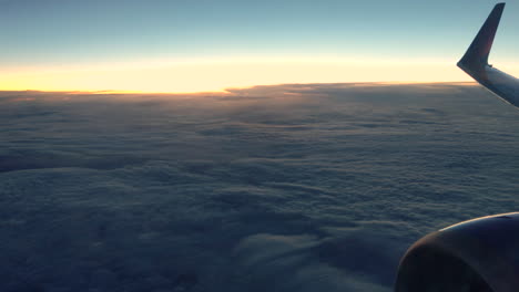 Shot-of-an-airplane-engine-and-wing-flying-on-top-of-the-clouds-as-the-sun-sets-in-the-horizon