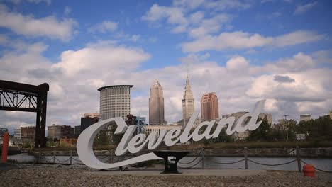 Cleveland,-Ohio-Skriptzeichen-An-Einem-Sonnigen-Tag-Mit-Wolken,-Die-An-Einem-Blauen-Himmel-Vorbeiziehen,-Und-Ein-Frachtschiff-Fährt-Vorbei
