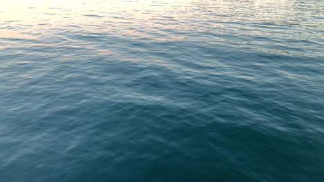 Ruhiges-Meer-Ohne-Wellen,-Dunkles-Wasser-Schwingt-Sanft-Am-Horizont,-Eine-Kleine-Reflektion-Der-Sonne-Oben-Links
