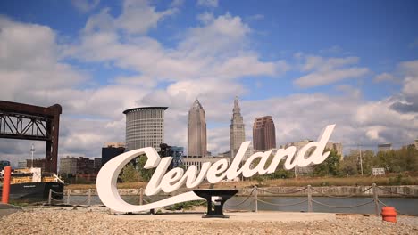 Cleveland,-Ohio-script-sign-on-a-sunny-day-with-clouds-passing-by-a-blue-sky-and-a-cargo-shipping-freighter-passes-by