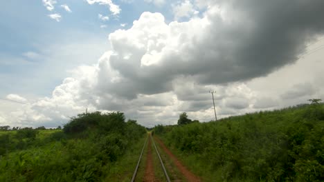 Un-Punto-De-Vista-En-Cámara-Lenta-Tomado-De-Un-Tren-Que-Se-Mueve-Lentamente-A-Lo-Largo-De-Una-Vía-Férrea-En-África-Rural-Mirando-Hacia-Las-Nubes