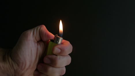 Close-view-of-hand-holding-a-lighter-and-lighting-it-with-a-black-background