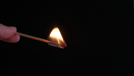 Hand-holding-a-burning-match-facing-down-with-a-black-background