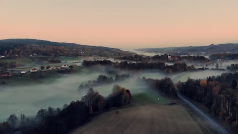 Aerial-over-road-cutting-through-misty-farmland-near-Bollebyggd,-Sweden
