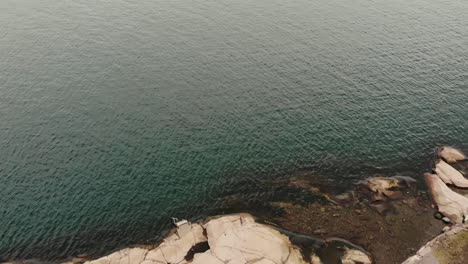 Overhead-aerial-over-the-rocky-shoreline-out-to-sea-near-Lysekil,-Sweden