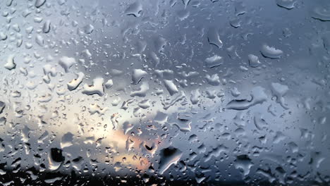 Close-up-of-raindrops-at-window,-blurred-sunset-in-background