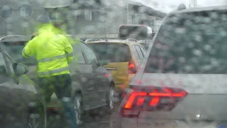 Cars-waiting-in-traffic-in-rainy-weather,-man-in-yellow-jacket-directing-the-drivers