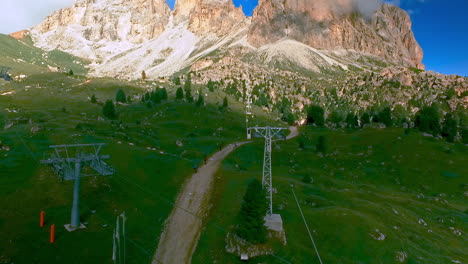 Drone-shot-of-the-Langkofel---Sassolungo-ropeway-with-hikers-and-mountain-bikers-on-the-path-below-and-the-peak-of-Langkofel-in-the-background