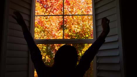 4K-footage-of-an-unidentifiable-woman-enjoying-the-beautiful-colors-of-autumn-foliage-outside-her-window-as-she-does-her-morning-stretch