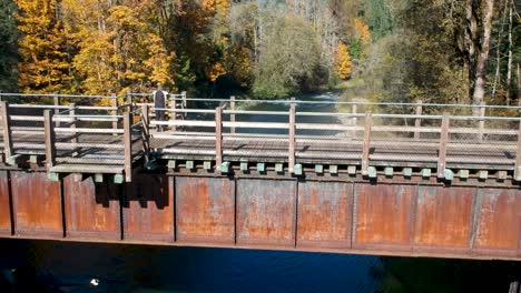 low-angle-revealing-drone-shot-of-lady-looking-at-view-on-old-wooden-rail-bridge-in-Canada-in-the-fall