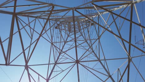 Electricity-transformer-tower-on-a-blue-sky-backdrop-with-electric-cable-wires-lines-underneath-look-up-view