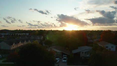 Aerial-view-ascending-over-the-suburbs-at-golden-hour,-with-the-sun-in-the-distance-setting-and-creating-a-beautiful-lens-flare
