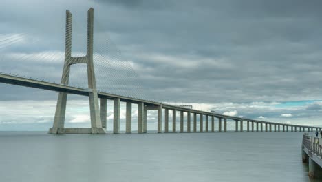 Timelapse-of-the-Vasco-da-Gama-bridge-in-Lisbon,-Portugal-on-a-cloudy-day-with-a-near-by-walkway