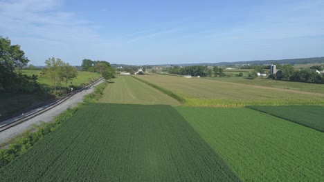 Aerial-View-Close-up-of-Green-Agricultural-Farm-Lands-Next-to-a-Rail-Road-Track-in-Amish-Countryside-on-a-Sunny-Summer-Day