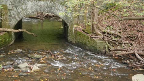 Water-stream-going-under-stone-bridge,-near-Covered-Bridge,-Thomas-Mill-at-Wissahickon-Creek