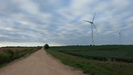 POV-while-driving-on-a-rural-gravel-road-watching-a-turning-wind-turbine-that-is-in-a-soybean-field-along-a-gravel-road-in-rural-Nebraska-USA-on-a-cloudy-day