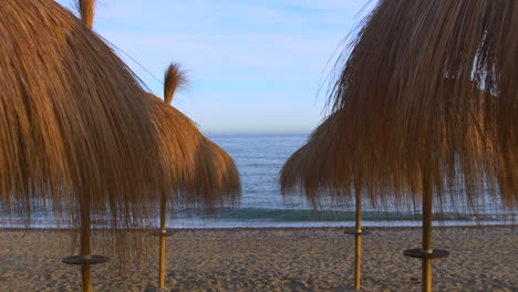 4k-gimbal-shot-gliding-through-straw-umbrellas-on-a-beach-in-Marbella,-Malaga,-Spain,-costa-del-sol-dream-holiday-location