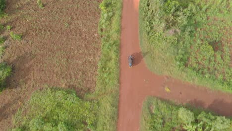 Aerial-birds-eye-view-shot-of-a-African-man-on-a-motorcycle-riding-on-a-dirt-road-through-rural-Africa