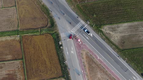Top-down-rotating-view-of-the-vehicles-driving-through-intersection-between-rice-field-farm