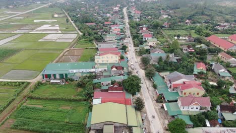 Aerial-shot-of-nice-rural-village-with-a-wide-rice-farm-field-at-the-left-side-and-straight-highway-in-the-middle