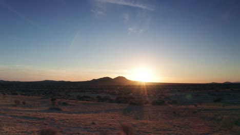 Bright-sun-on-horizon-casting-light-rays-over-golden-Mojave-Desert,-Dolly-Left