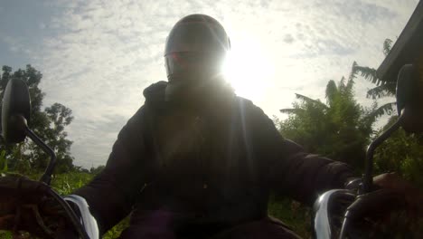 A-action-shot-of-an-African-man-wearing-a-helmet-while-steering-a-motor-bikes-handle-bars-rides-through-rural-Africa-with-the-sun-shining-behind